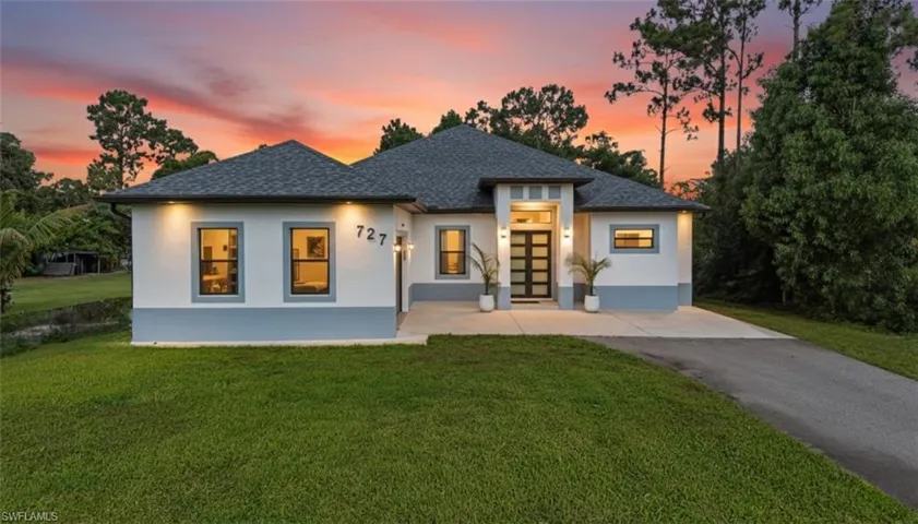 View of front of house with stucco siding, a lawn, a shingled roof, and driveway