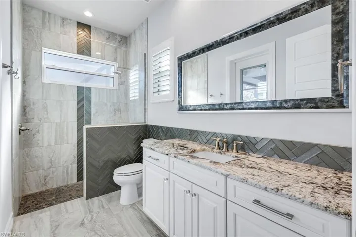 Bathroom featuring walk in shower, vanity, plenty of natural light, tile walls, and custom tile flooring