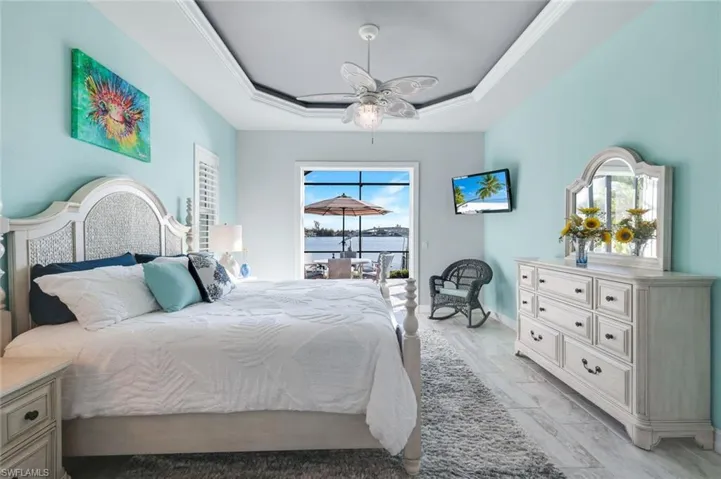 Primary Bedroom featuring access to the lanai and pool area, custom ceiling fan, crown molding, and a tray ceiling