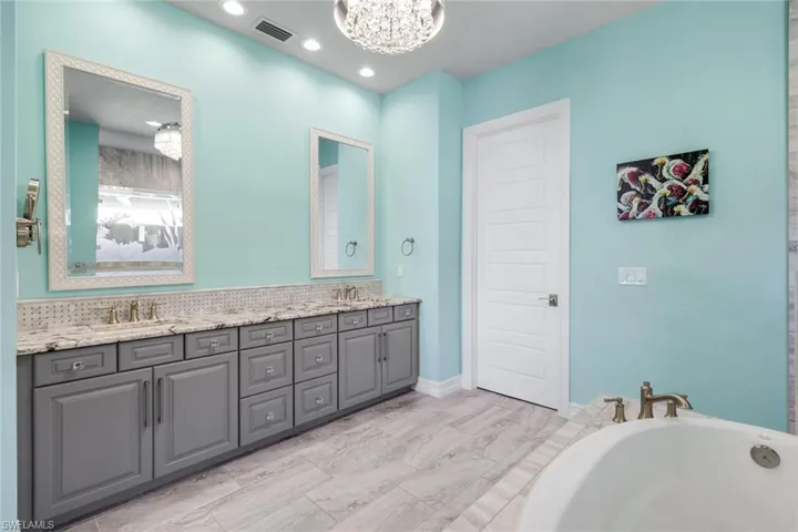 Bathroom with double vanity, a custom chandelier, a tub, recessed lighting and custom mirrors