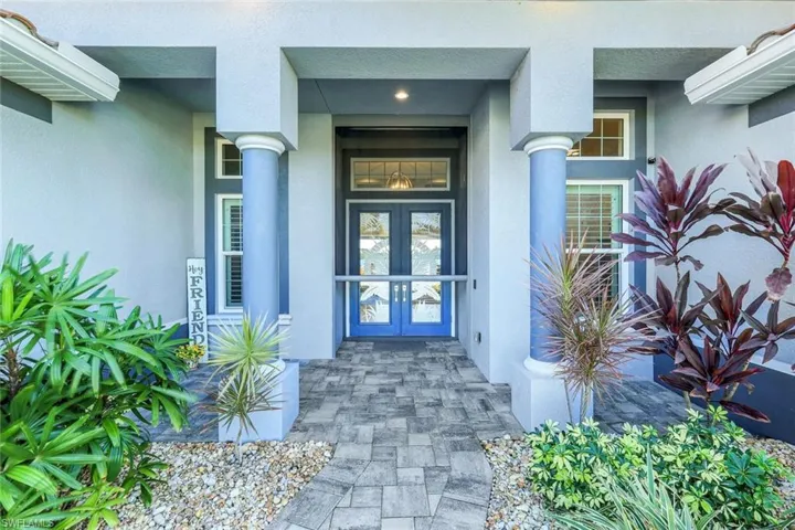 Front entry to property with french double doors w/ impact protection and stucco siding.  Auto-roll down screen allow open doors for airflow throughout if desired.
