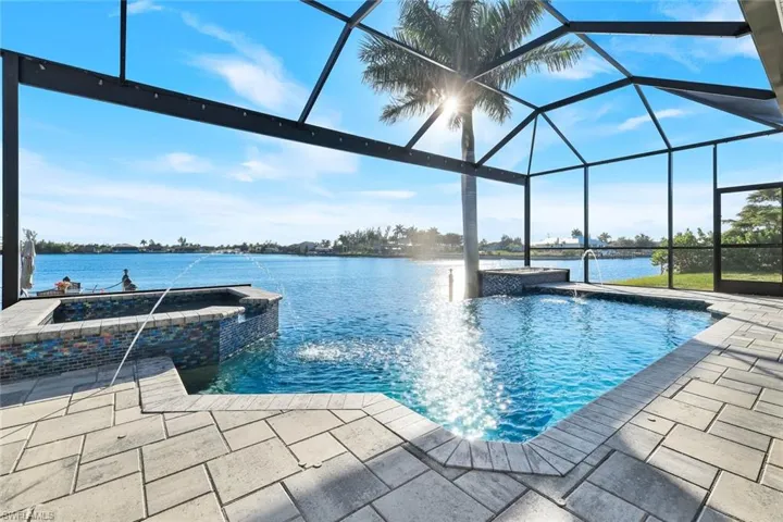 View of pool featuring panoramic screen enclosure, a heated salt-water pool with connected spa, a water view and paver pool deck and lanai