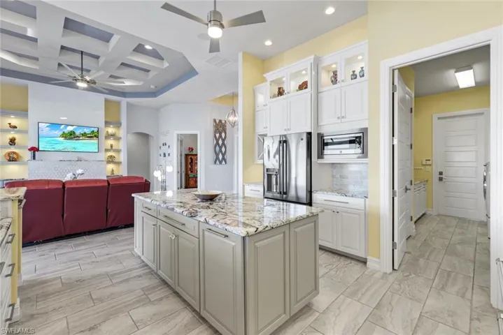 Kitchen with open floor plan, coffered ceiling, light stone countertops, appliances with stainless steel finishes, and arched walkways