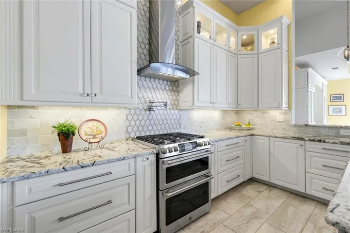 Kitchen featuring double oven gas range, granite counters, wall chimney range hood, and white cabinetry