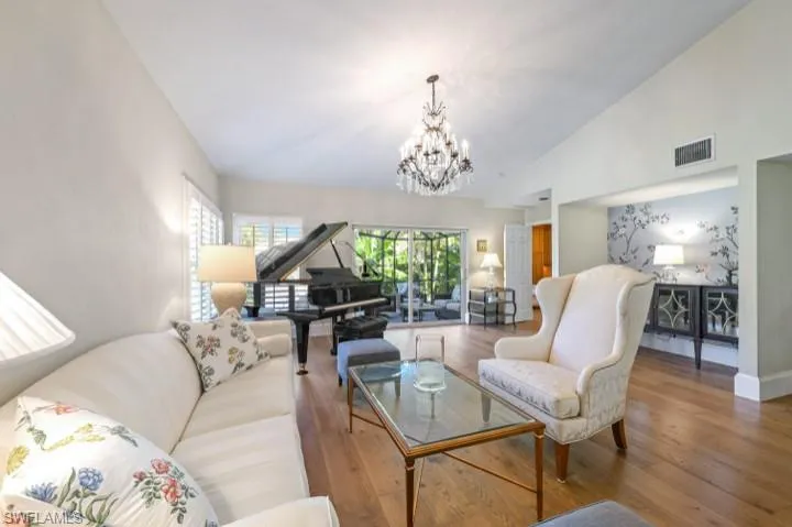 Spacious Great Room featuring new hurricane impact slider doors, wood floors, volume ceiling and plantation shutters throughout