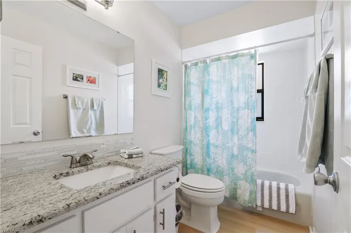 Full bath with decorative backsplash, shower / bath combination with curtain, wood finished floors, vanity, and toilet
