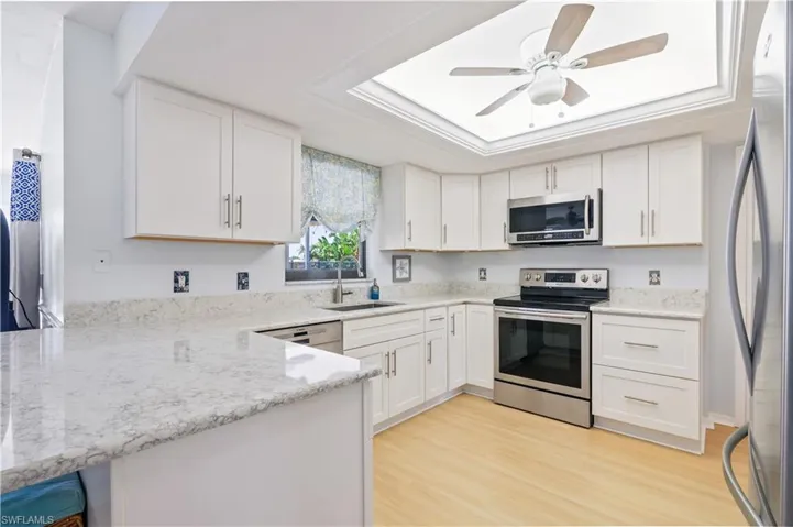 Kitchen with a sink, white cabinetry, a tray ceiling, and stainless steel appliances