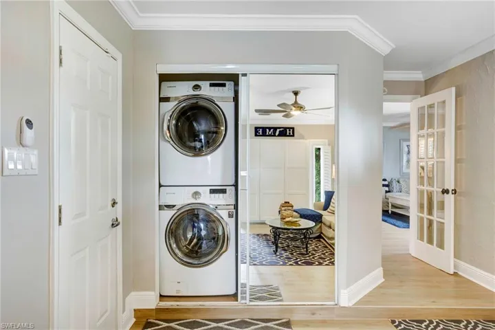 Clothes washing area with wood-type flooring, ornamental molding, french doors, and stacked washer / dryer