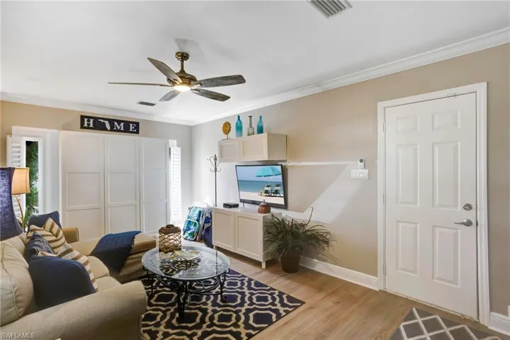 Living room with ceiling fan, ornamental molding, and light wood-type flooring