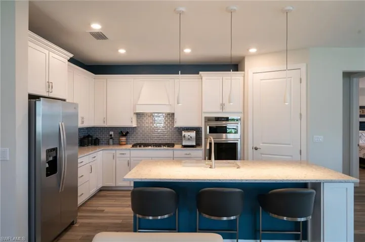 Kitchen featuring stainless steel appliances, dark wood-type flooring, custom exhaust hood, a kitchen bar, and white cabinets