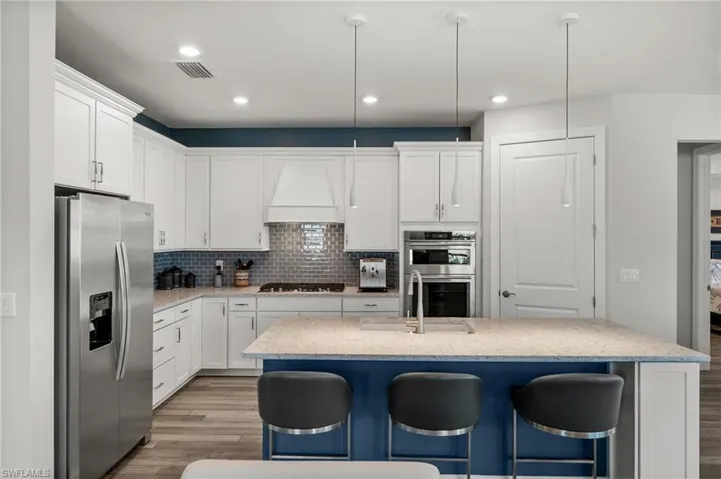 Kitchen with stainless steel appliances, light wood-type flooring, custom range hood, a kitchen breakfast bar, and white cabinets