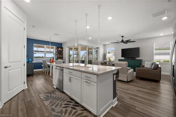 Kitchen with dishwasher, white cabinets, dark wood-style floors, an island with sink, and light stone counters