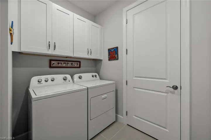 Washroom featuring washing machine and clothes dryer, cabinet space, and light tile patterned floors