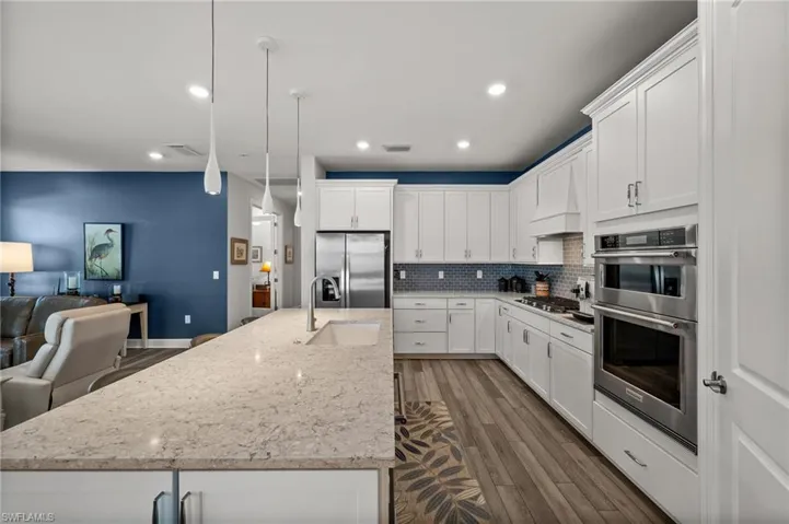 Kitchen featuring appliances with stainless steel finishes, open floor plan, decorative backsplash, custom range hood, and dark wood-type flooring