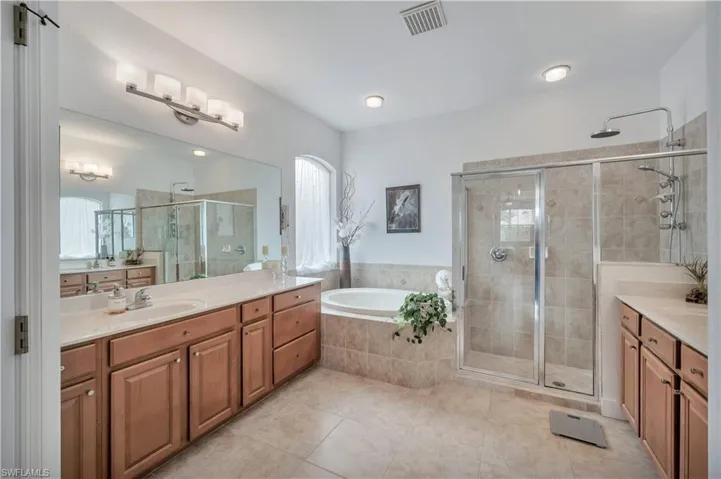 Full bath with two vanities, a shower stall, a bath, and light tile patterned flooring