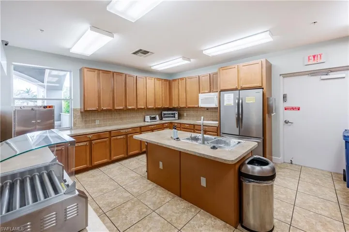 Kitchen with light countertops, backsplash, stainless steel appliances, light tile patterned flooring, and an island with sink