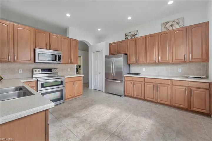 Kitchen with stainless steel appliances, tasteful backsplash, arched walkways, recessed lighting, and light tile patterned flooring