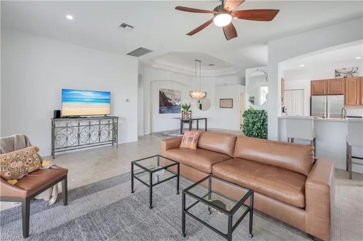 Living room with a raised ceiling, a ceiling fan, light tile patterned floors, and recessed lighting