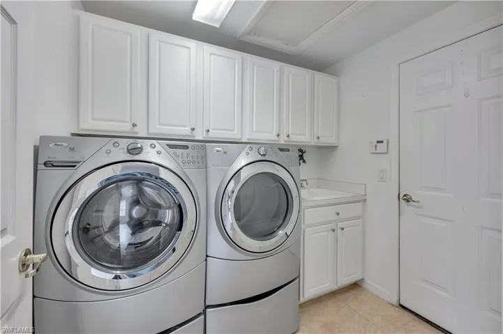 Laundry area with light tile patterned floors, washer and clothes dryer, and cabinet space