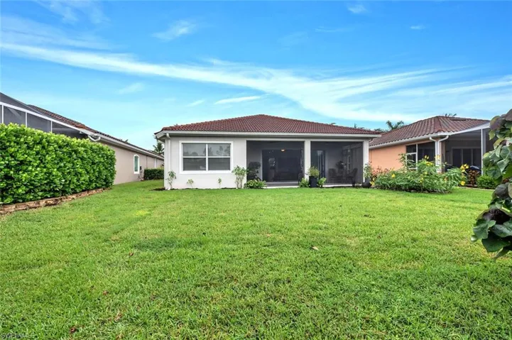 Rear view of property featuring a lawn, a tiled roof, a sunroom, and stucco siding