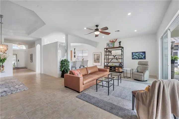 Living area with arched walkways, light tile patterned flooring, ceiling fan, recessed lighting, and a chandelier