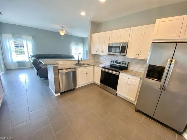 Kitchen featuring ceiling fan, sink, appliances with stainless steel finishes, kitchen peninsula, and backsplash