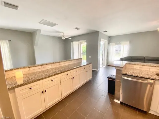 Kitchen featuring tasteful backsplash, white cabinets, dishwasher, ceiling fan, and light stone countertops