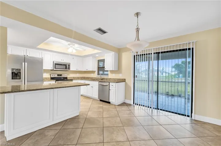 Kitchen featuring appliances with stainless steel finishes, white cabinets, ornamental molding, decorative light fixtures, and dark stone counters