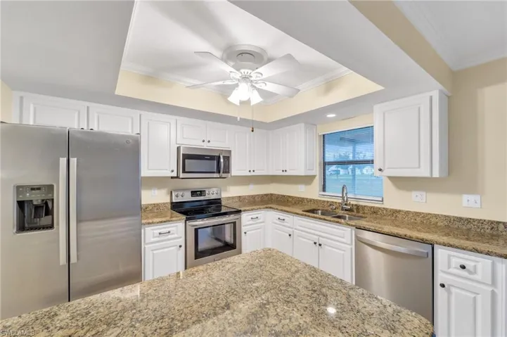 Kitchen featuring stainless steel appliances, white cabinetry, light stone countertops, a raised ceiling, and ornamental molding