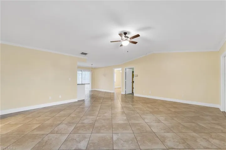 Empty room featuring crown molding, a ceiling fan, light tile patterned floors, and vaulted ceiling