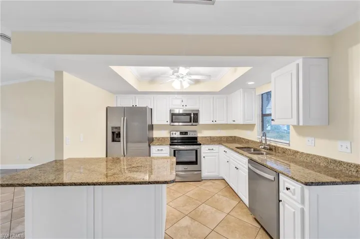 Kitchen featuring dark stone counters, appliances with stainless steel finishes, white cabinets, crown molding, and light tile patterned floors