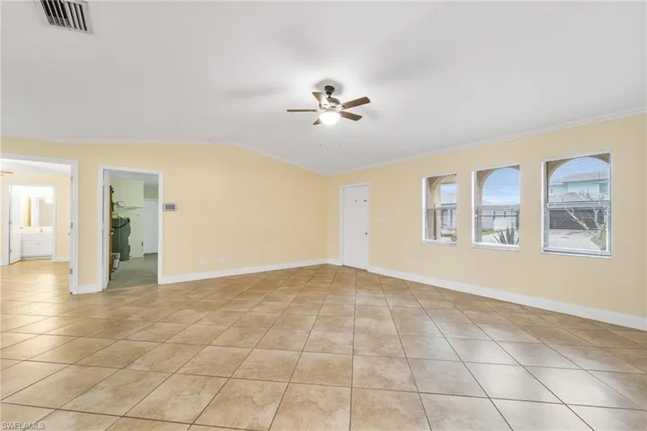Empty room with vaulted ceiling, crown molding, ceiling fan, and light tile patterned flooring