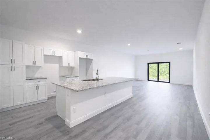 Open-concept kitchen and living area featuring white cabinetry, light-toned granite countertops, and a central island with a stainless steel sink