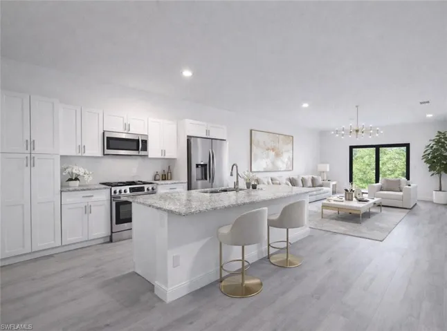 Open-concept living area featuring a kitchen with white cabinetry, stainless steel appliances, and a central island with a light-toned countertop