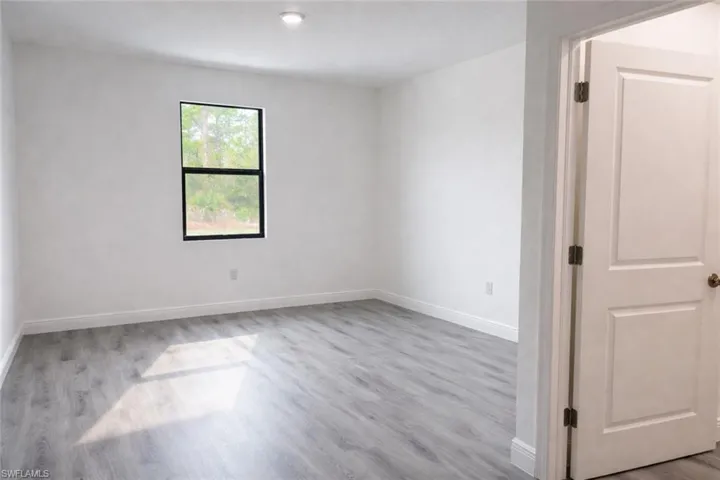 Spacious room featuring light wood-finish flooring, white baseboards, and a single recessed ceiling light