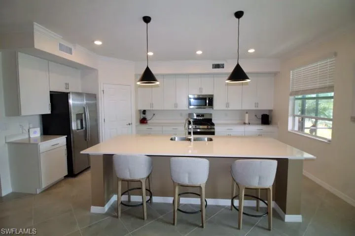 Kitchen featuring stainless steel appliances, white cabinets, and a center island with sink