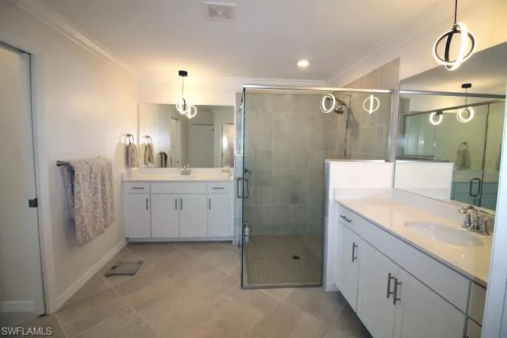 Bathroom featuring tile flooring, dual vanities, ornamental molding, and a solid glass shower