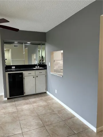 Bar featuring ceiling fan, sink, white cabinetry, and light tile patterned floors