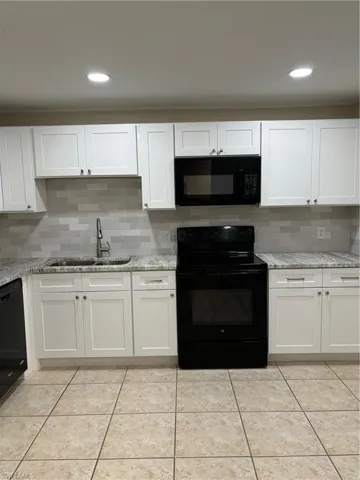 Kitchen with tasteful backsplash, sink, range, dishwashing machine, and white cabinets
