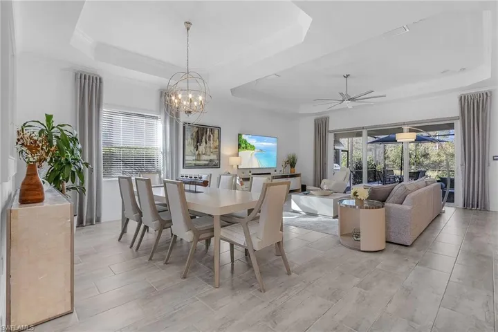 Dining room with ceiling fan with notable chandelier and a raised ceiling