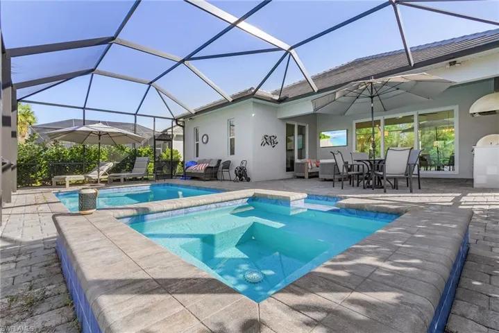 View of swimming pool featuring a patio area, an in ground hot tub, and glass enclosure