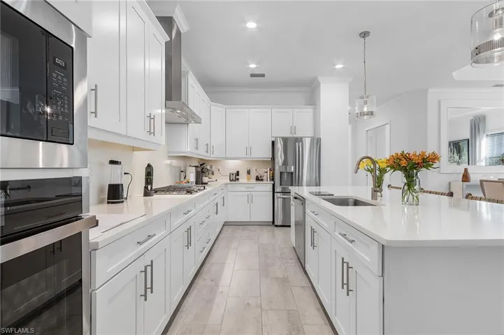 Kitchen with wall chimney range hood, white cabinetry, stainless steel appliances, pendant lighting, and sink