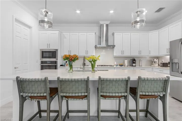 Kitchen featuring stainless steel appliances, wall chimney exhaust hood, a center island with sink, and white cabinets