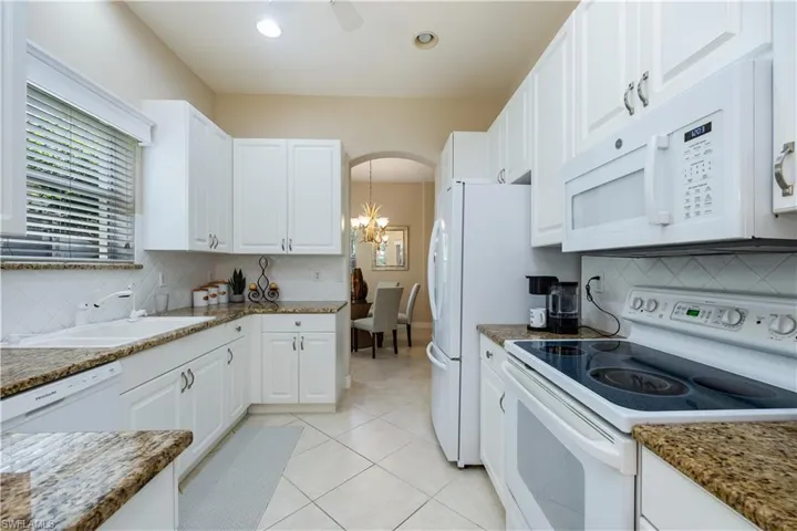 Kitchen with white appliances, white cabinetry, light tile patterned flooring, tasteful backsplash, and arched walkways