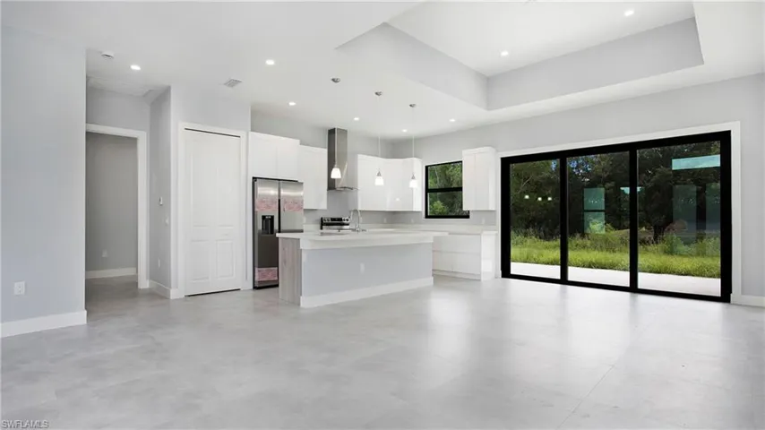 Kitchen featuring stainless steel refrigerator with ice dispenser, a kitchen island with sink, light countertops, white cabinets, and wall chimney range hood