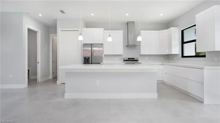 Kitchen featuring wall chimney range hood, stainless steel appliances, modern cabinets, concrete flooring, and white cabinets