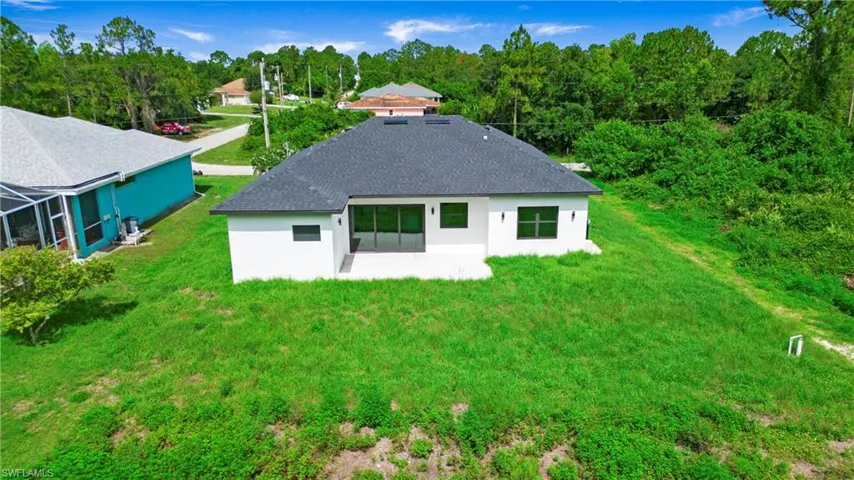 Back of property featuring a patio area, stucco siding, a shingled roof, a lawn, and a wooded view