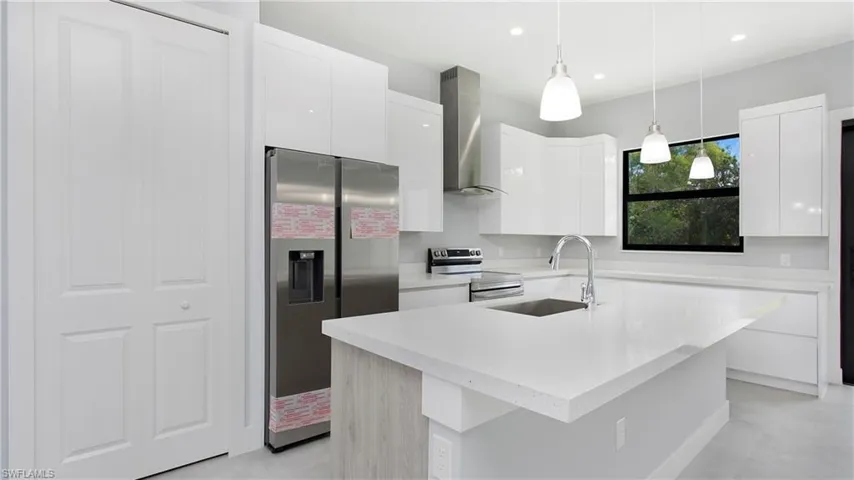 Kitchen with wall chimney exhaust hood, appliances with stainless steel finishes, modern cabinets, light countertops, and recessed lighting