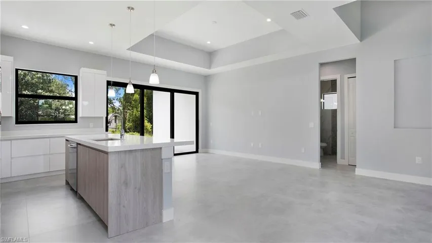 Kitchen with modern cabinets, white cabinetry, light countertops, a center island with sink, and decorative light fixtures