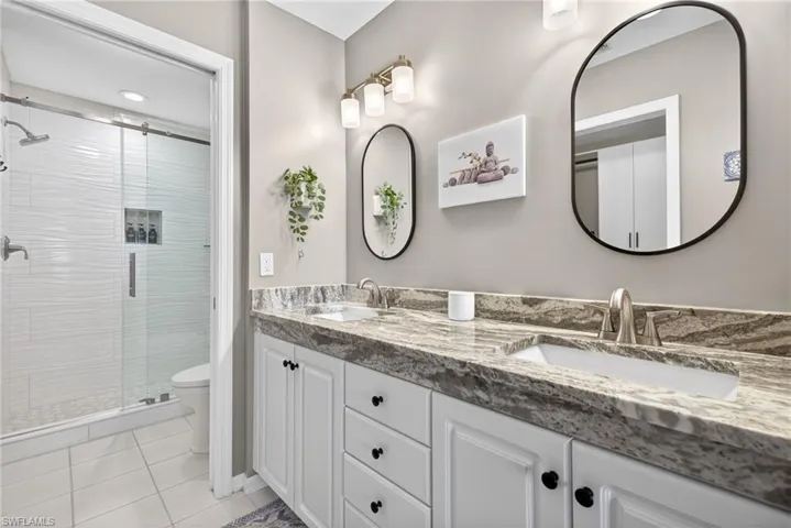 Bathroom with double vanity, a shower stall, and light tile patterned floors